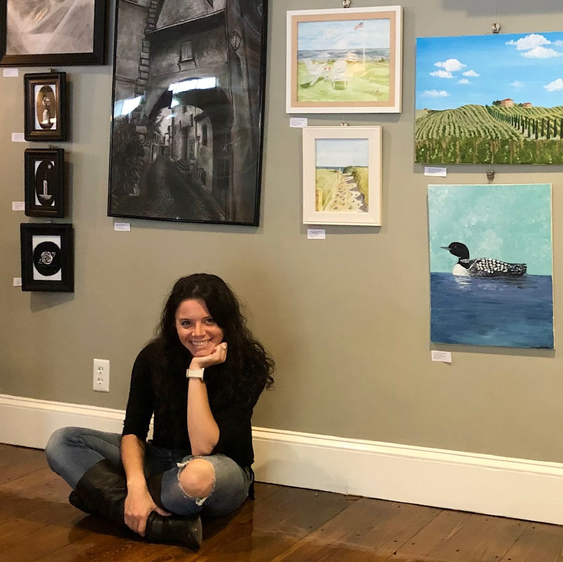 Woman sitting on the floor in front of a wall with various framed artworks.